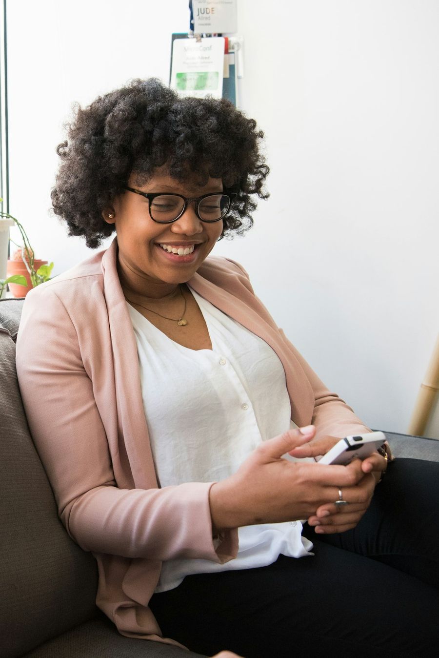 Mujer sonriendo mientras revisa su celular en el sofá