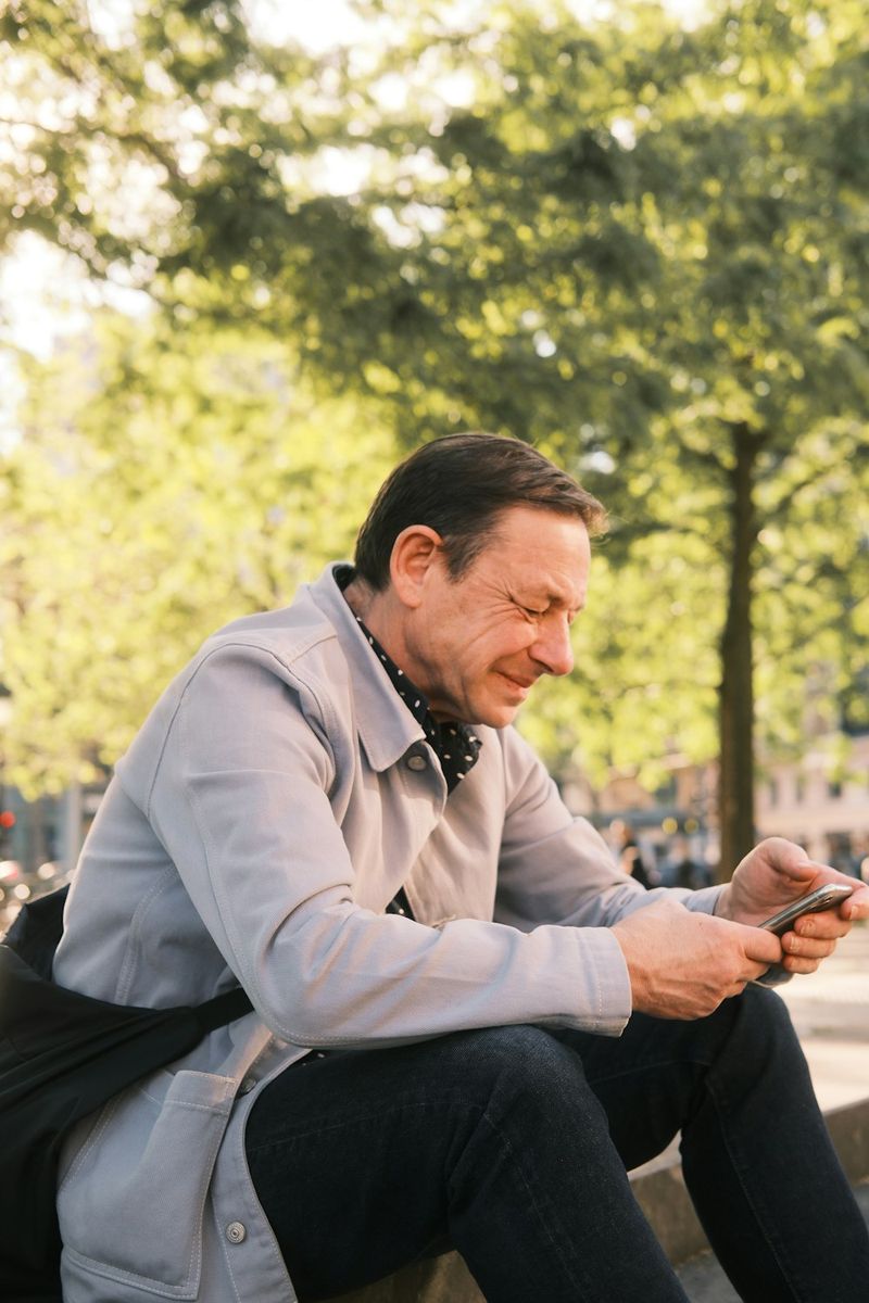 Hombre sonriendo a su celular, sentado en unas escaleras del parque